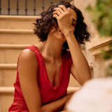 Woman in a red dress sitting on steps with her hand on her head.
