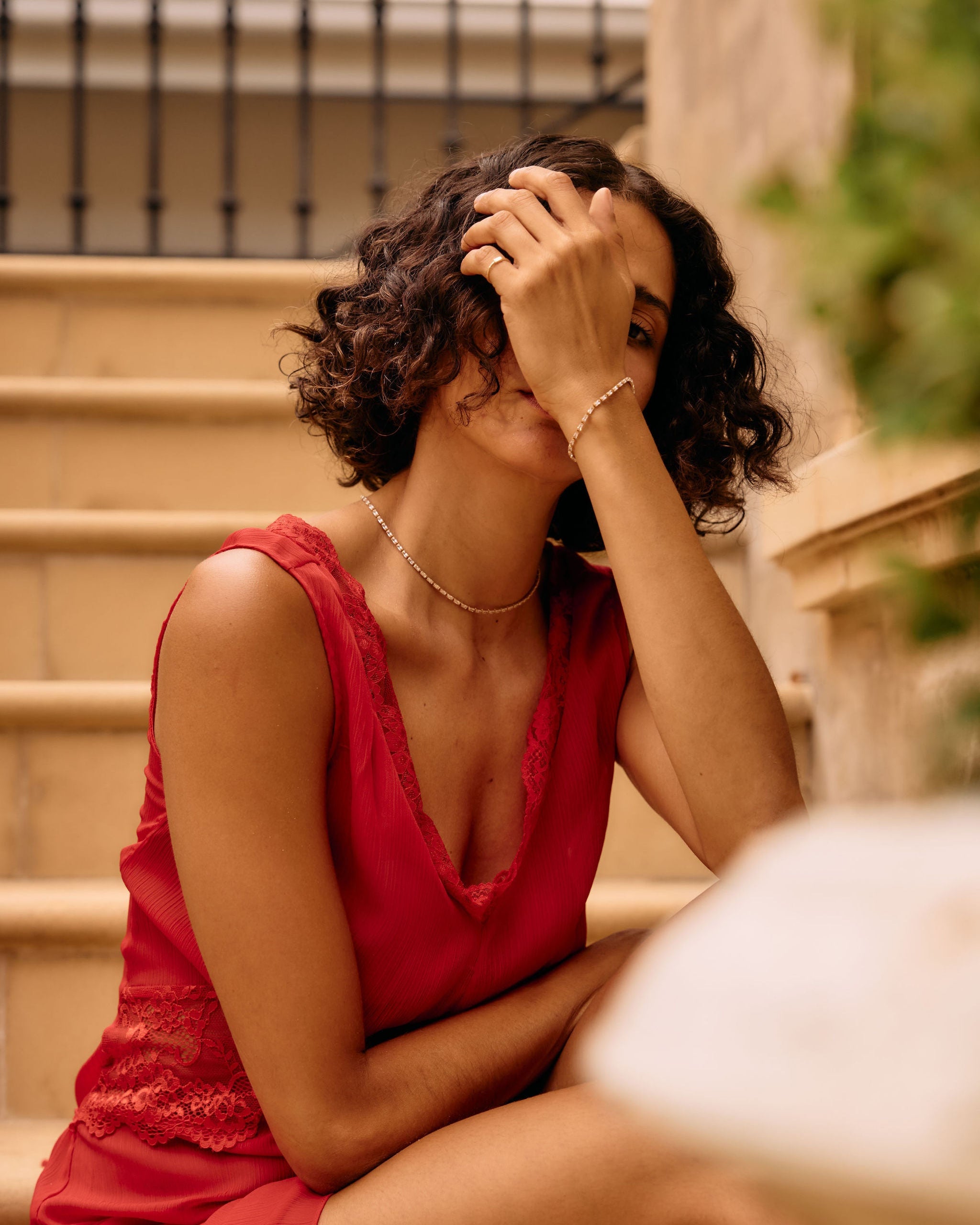 Woman in a red dress sitting on steps with her hand on her head.