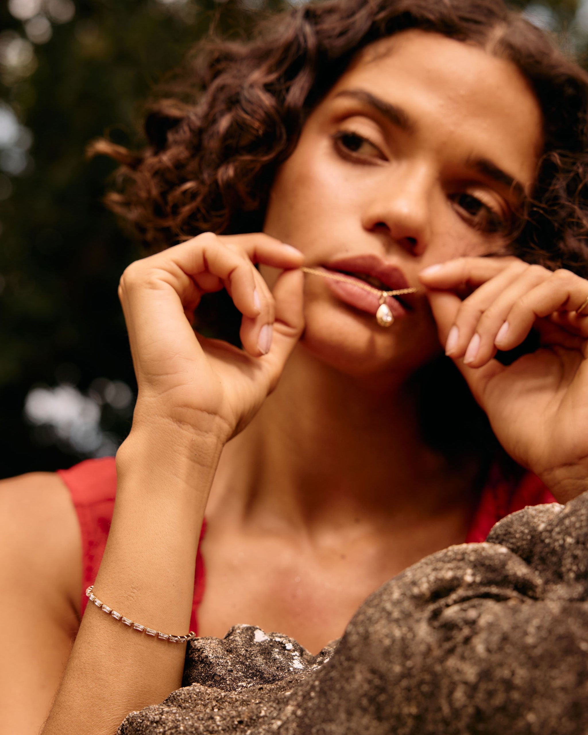 Woman with curly hair resting her chin on a stone surface outdoors