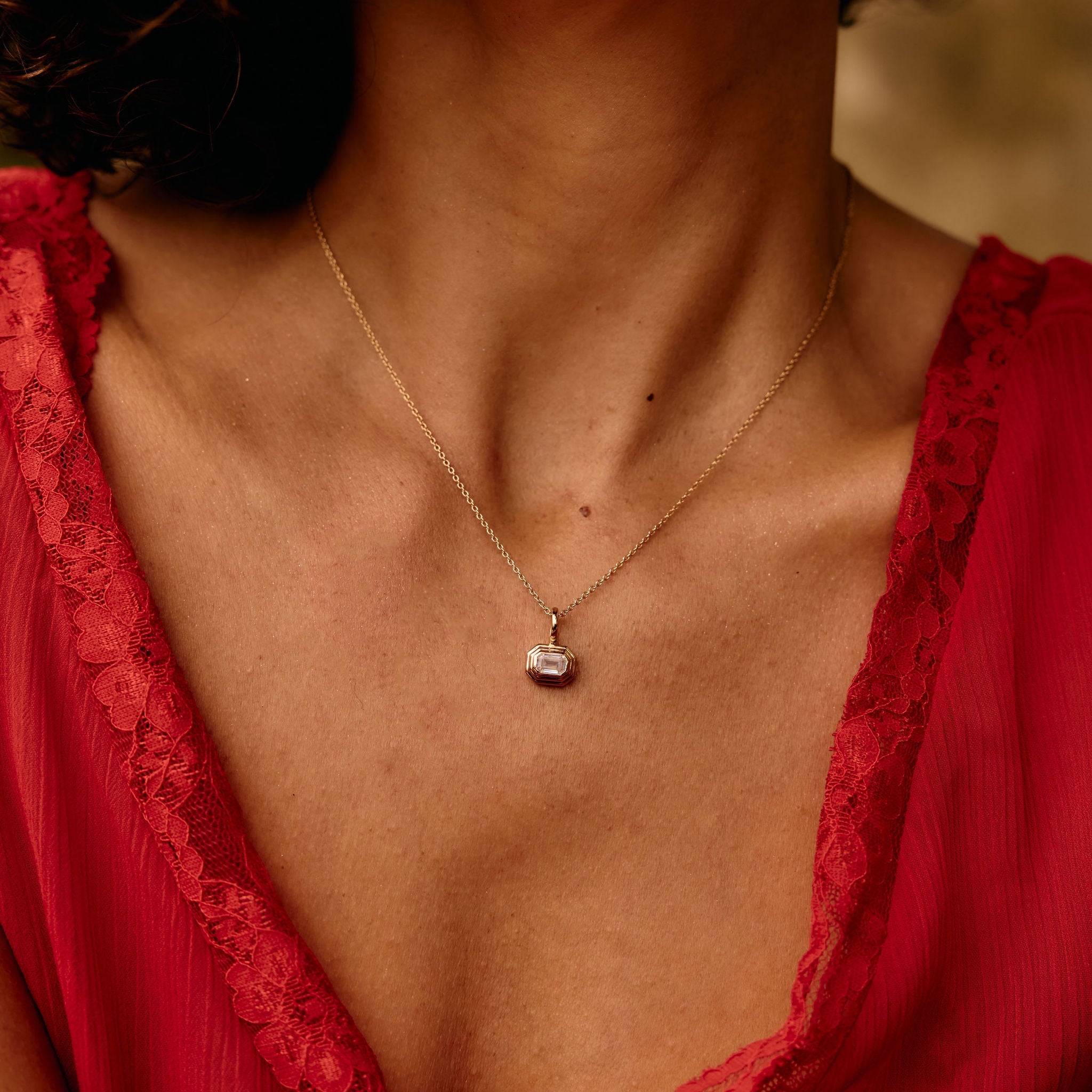 Close-up of a woman wearing a red lace garment and a gold necklace with a pendant.