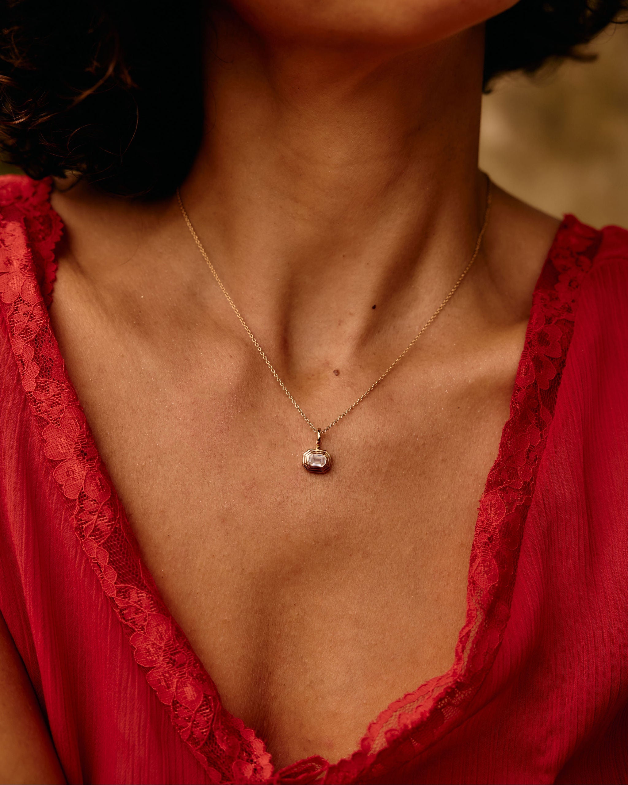 Close-up of a woman wearing a red lace garment and a gold necklace with a pendant.