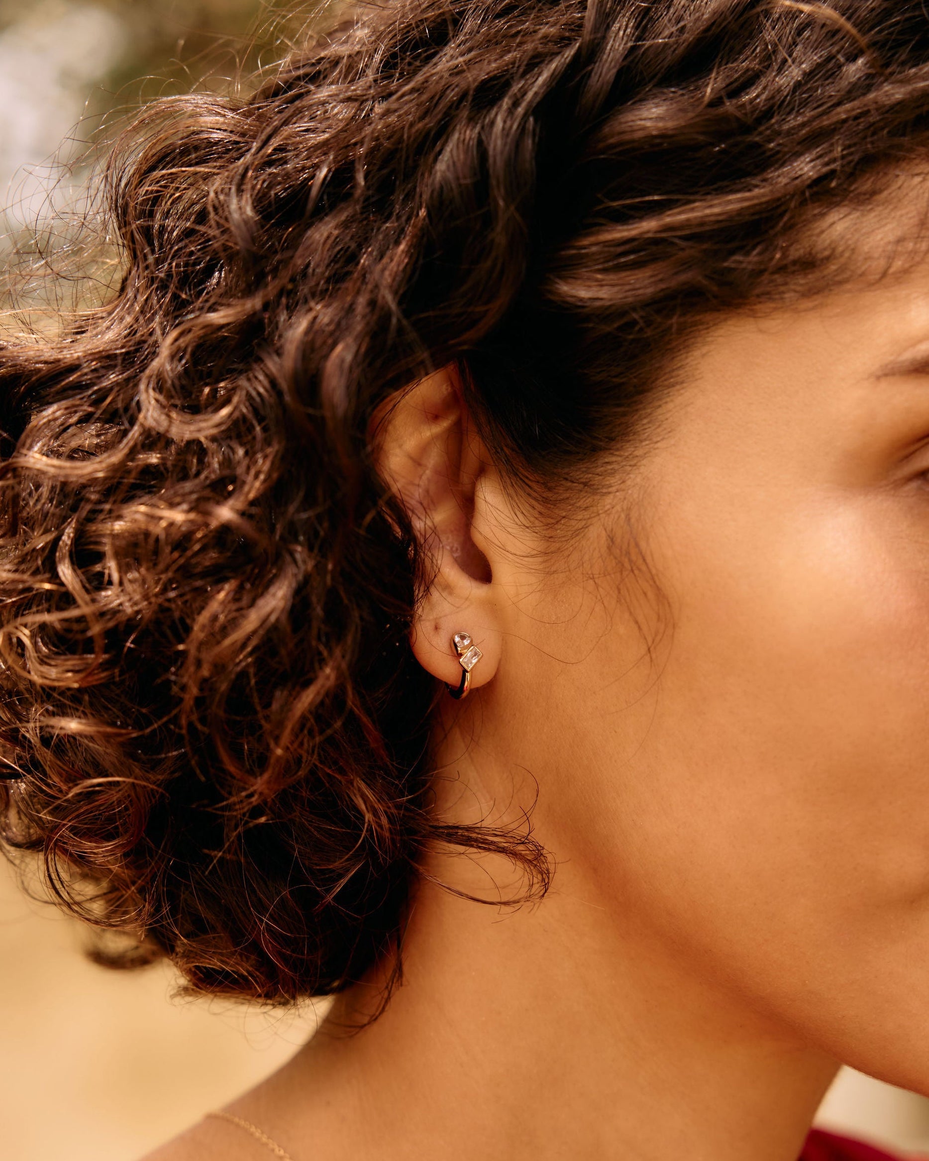 Close-up of a woman with curly hair and a red top, outdoors.