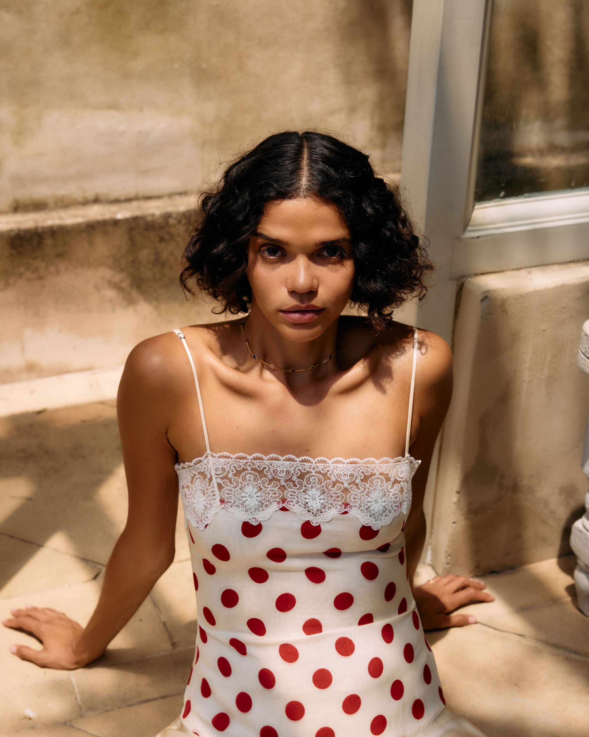 Woman wearing a polka dot dress sitting on a stone surface.