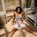 Woman in a polka dot dress sitting on a stone floor with a textured wall and bench in the background.