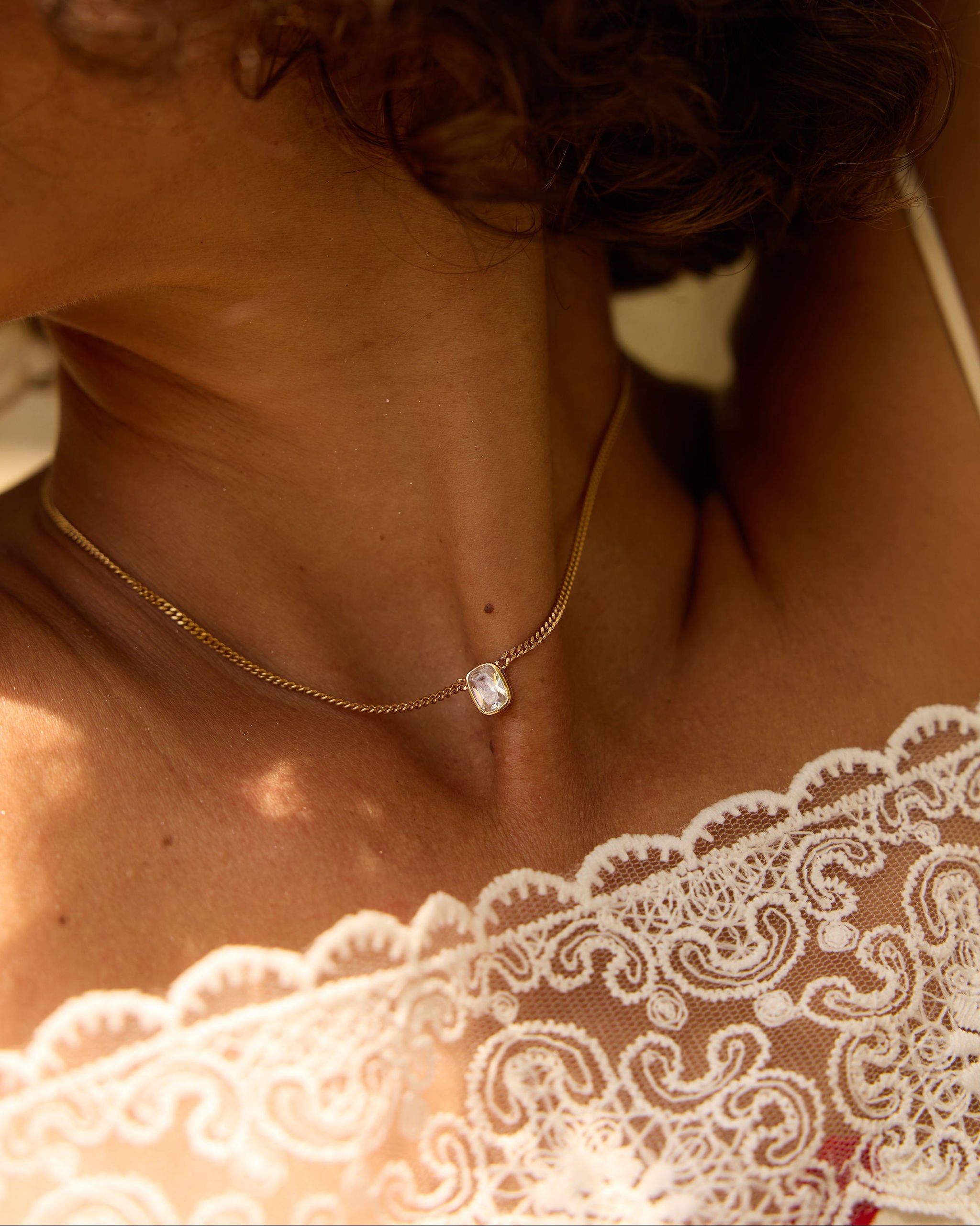 Close-up of a person wearing a gold necklace with a diamond pendant, focusing on the jewelry.
