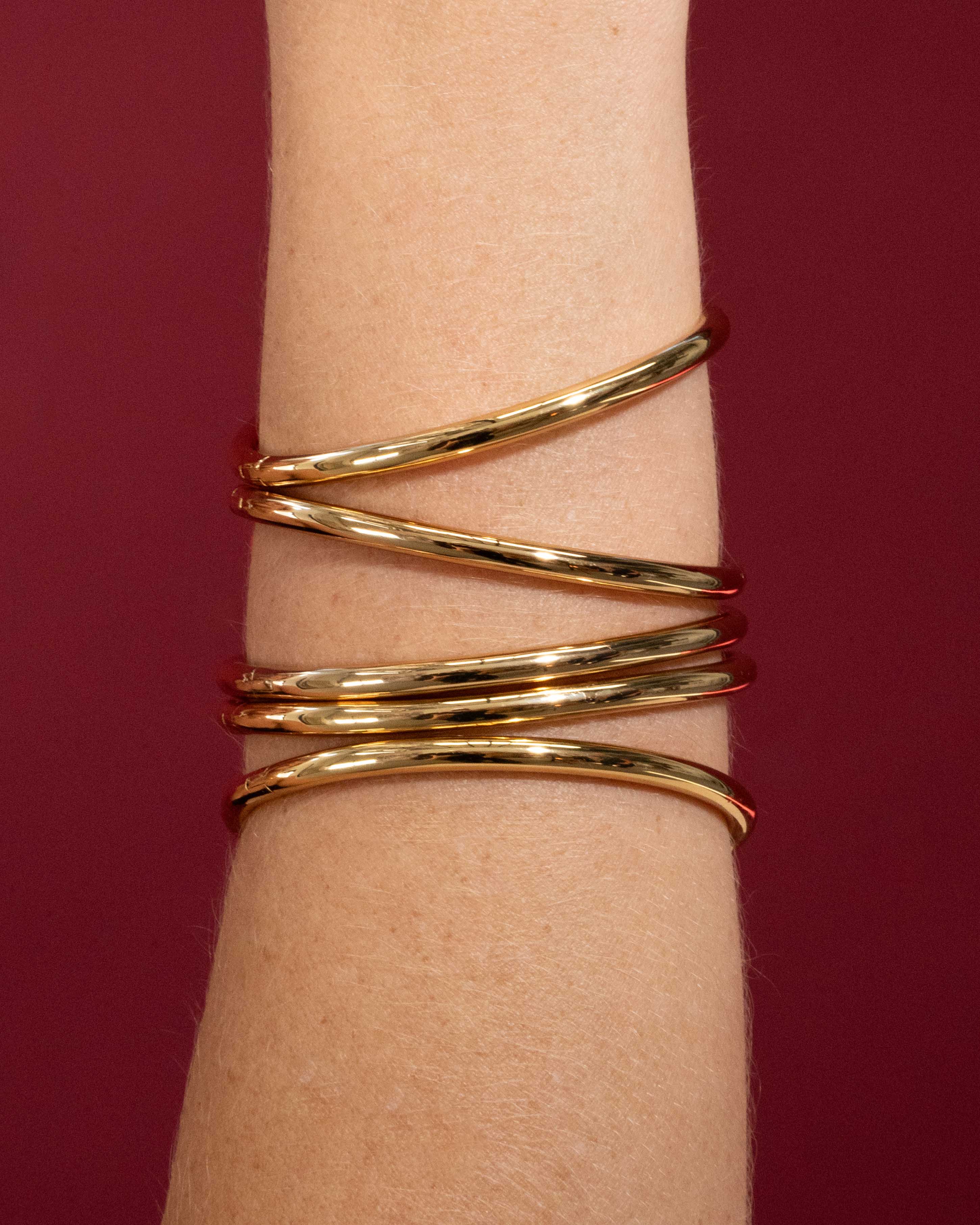 Gold bracelet on a wrist against a red background