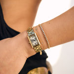 Gold watch and bracelet on a wrist with a blurred background