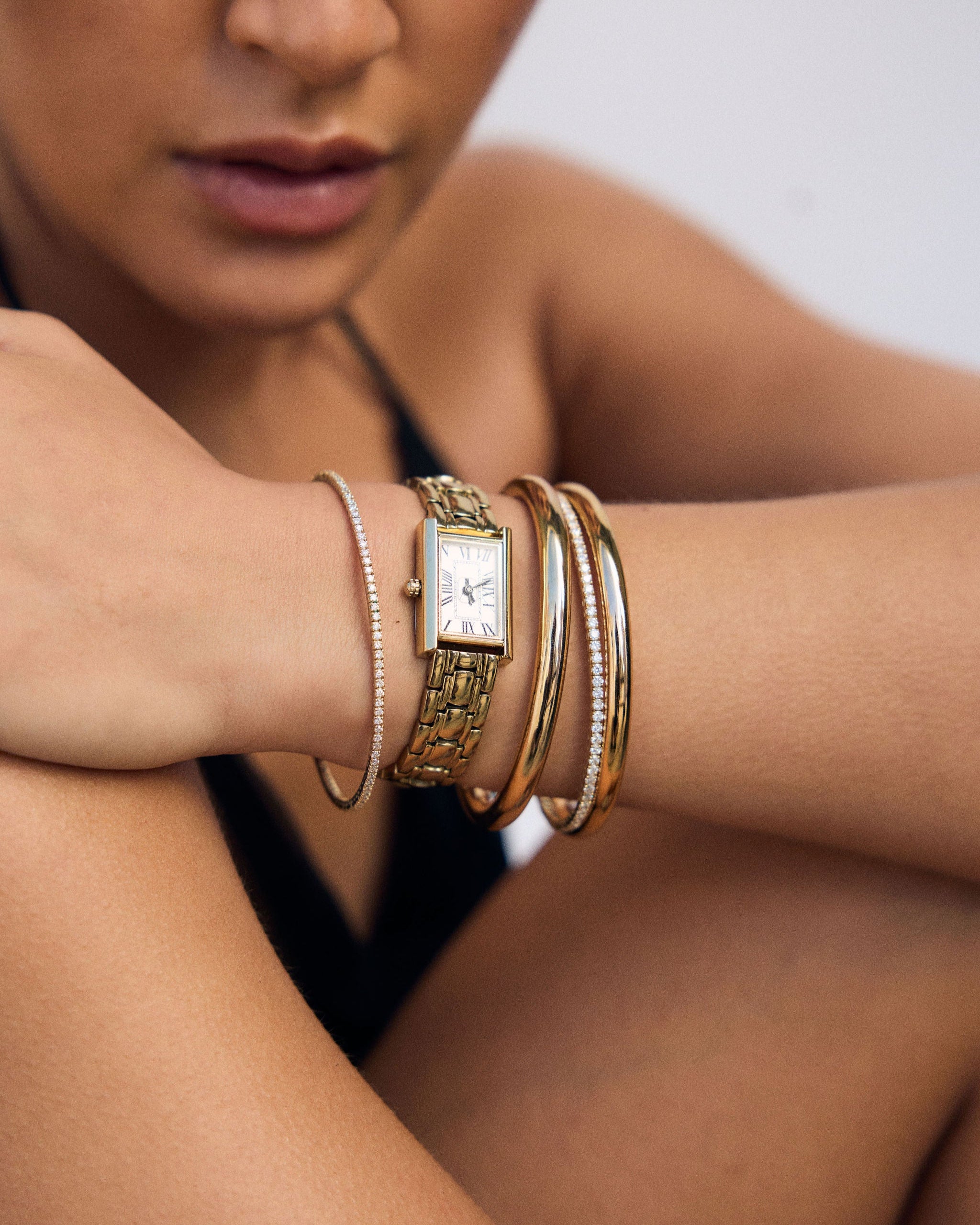 Close-up of a person's arm wearing a gold watch and bangles 