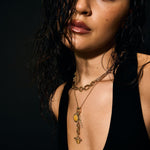 Woman wearing a black top and gold necklace against a dark background