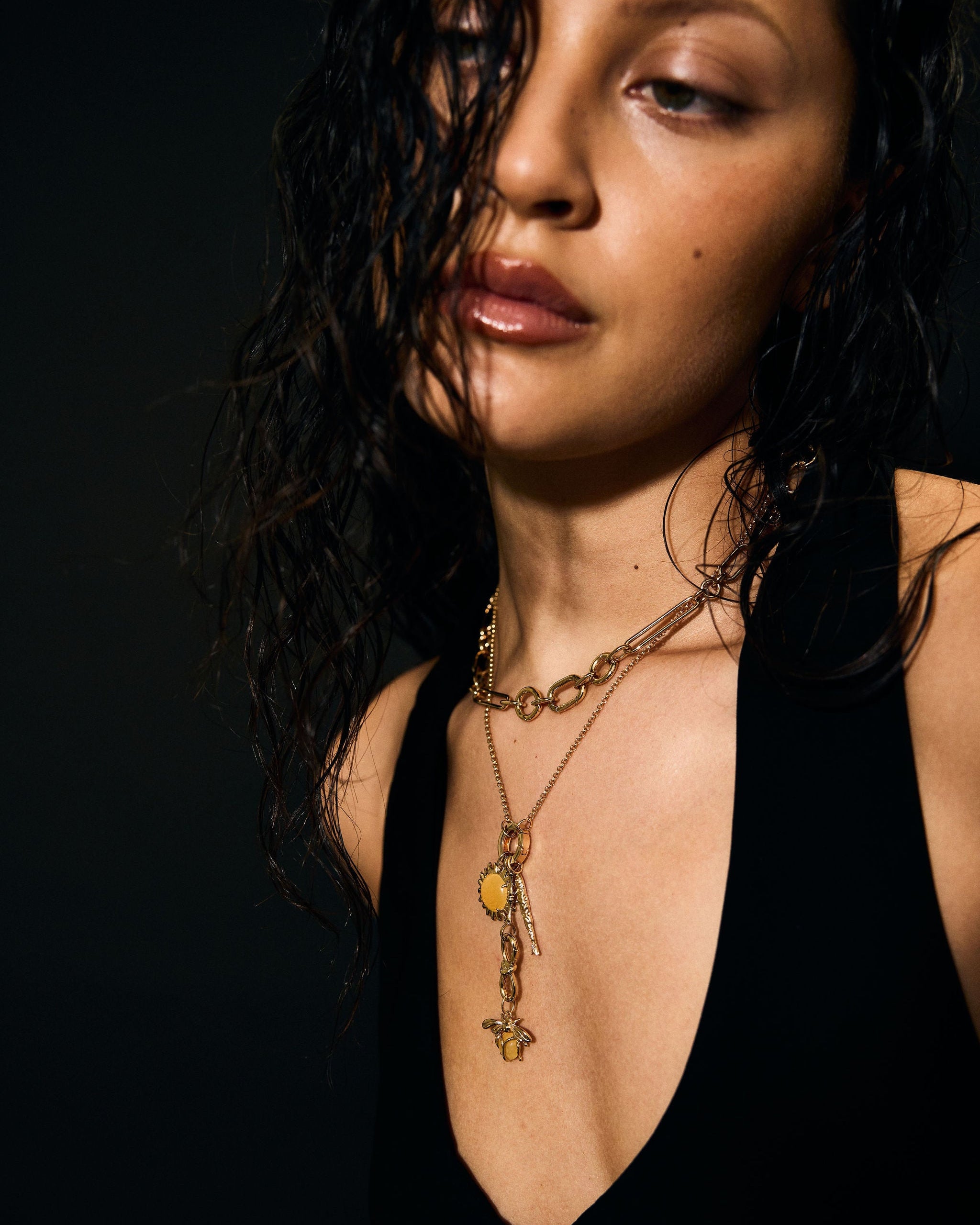 Woman wearing a black top and gold necklace against a dark background