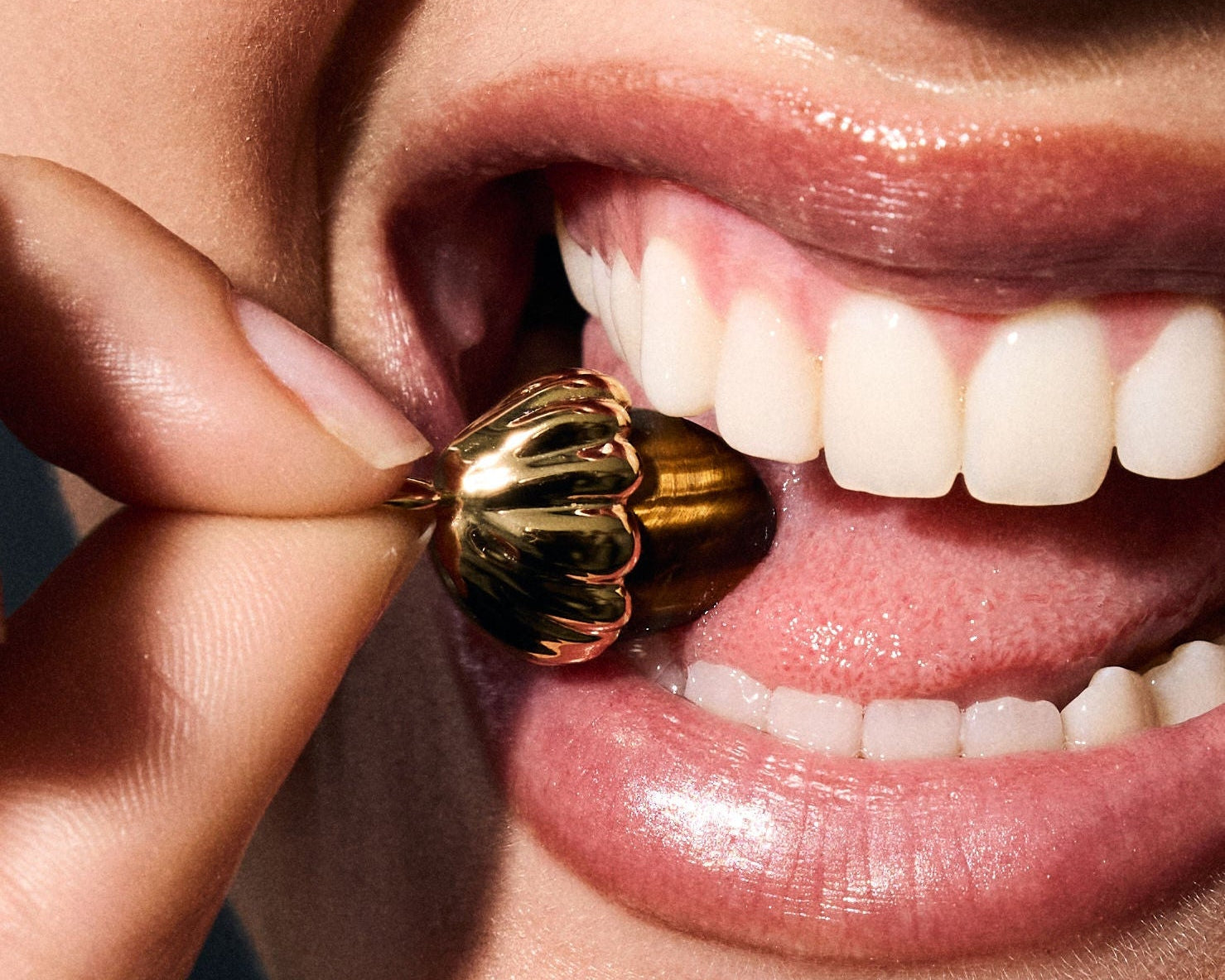 Close-up of a person holding a gold earring near their mouth.