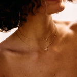 Close-up of a person wearing gold angel number necklaces with visible letters.