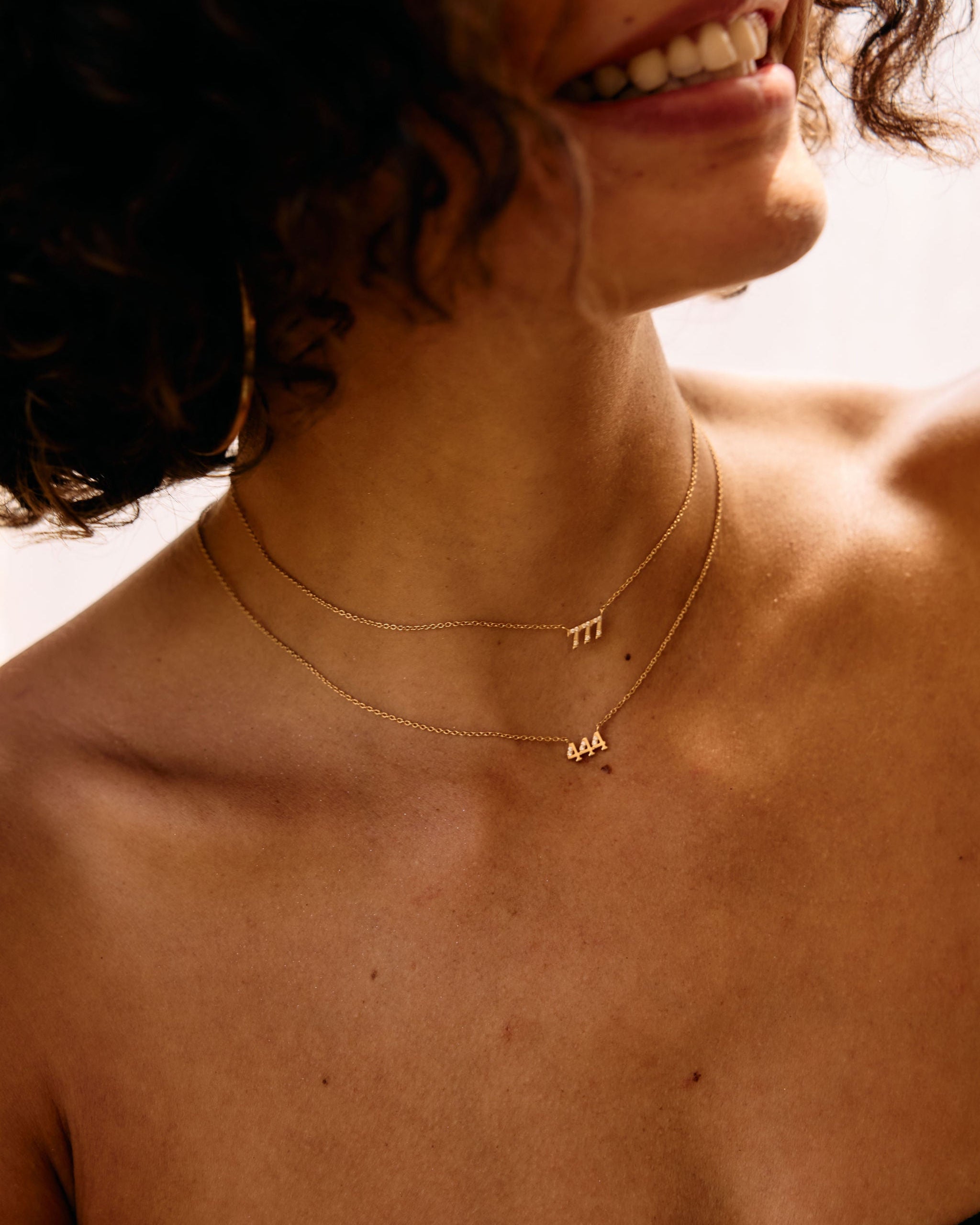 Close-up of a person wearing gold angel number necklaces with visible letters.
