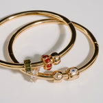 Gold bangles with gemstone accents on a light gray background