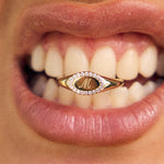 Close-up of a mouth wearing a gold ring with a letter 'M' on a blurred background