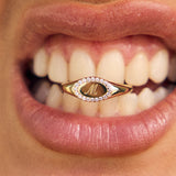Close-up of a mouth wearing a gold ring with a letter 'M' on a blurred background