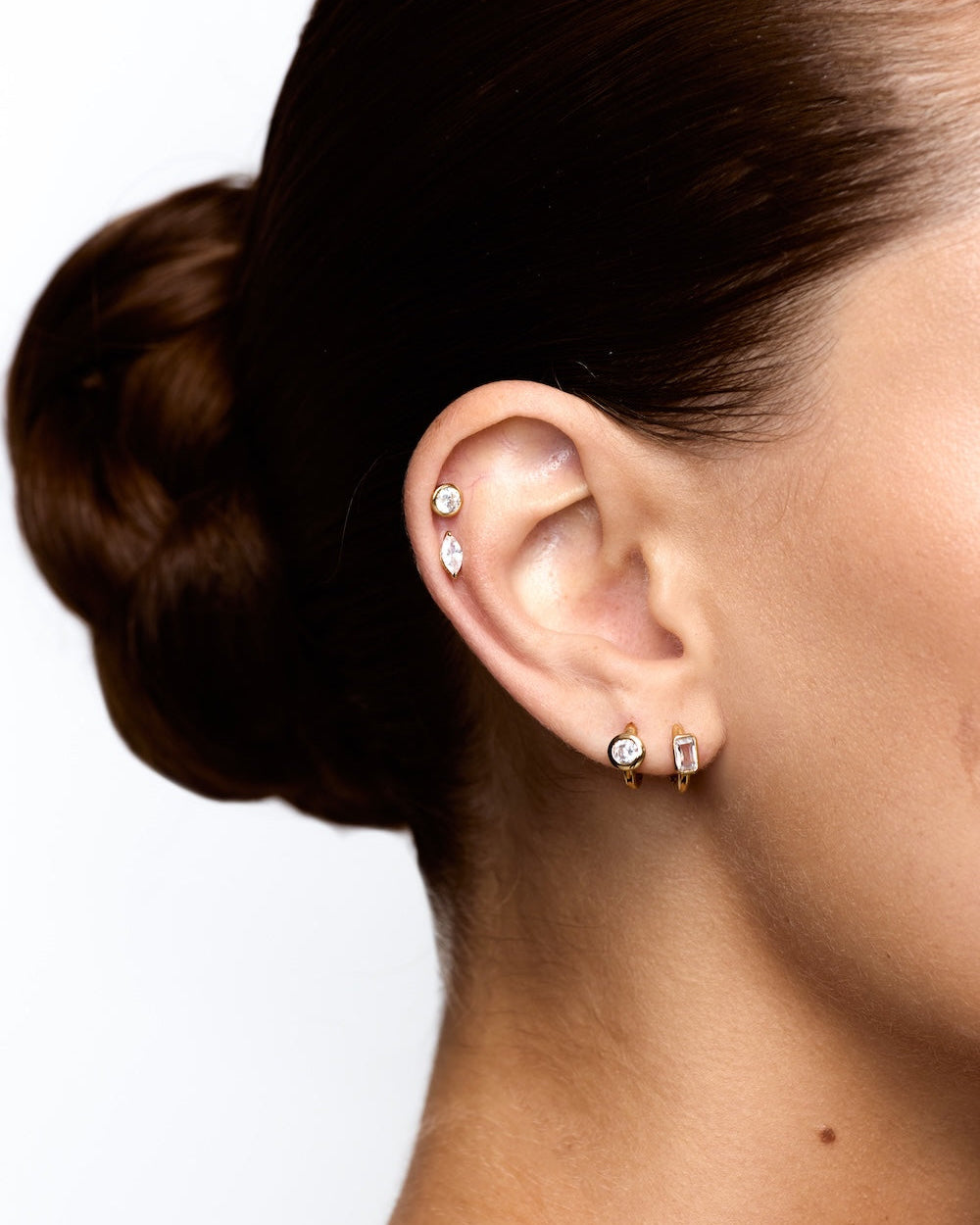 Close-up of an ear with diamond stud earrings on a white background