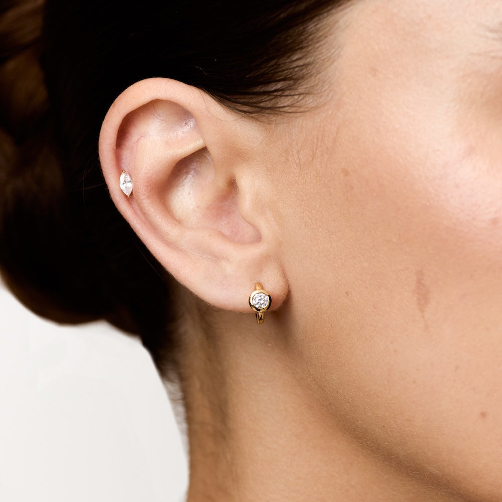 Close-up of a person wearing diamond stud earrings with a neutral background
