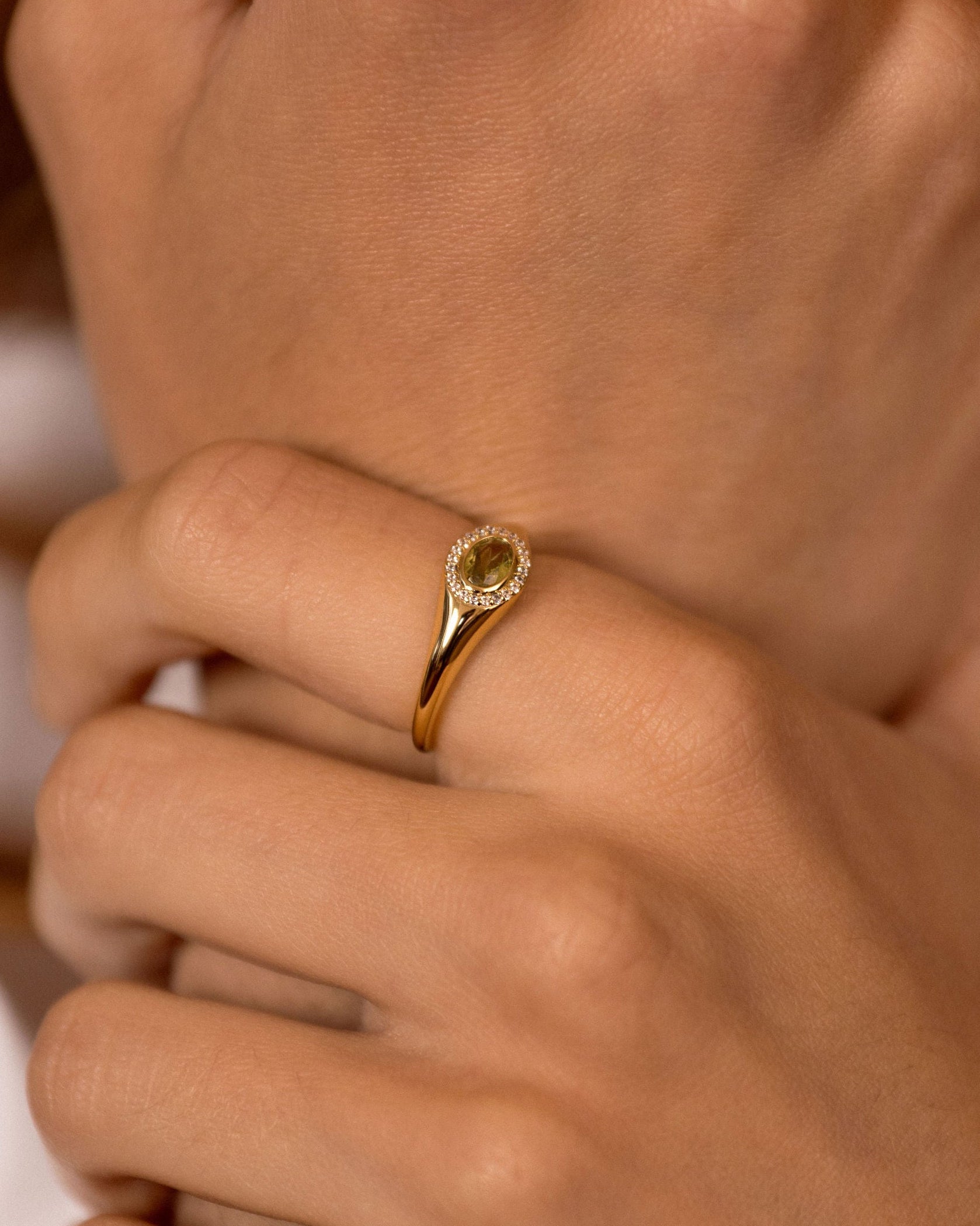 Close-up of hands wearing gold rings, including a ring with a round yellow gemstone and another with a dark oval gemstone, on warm skin tones.