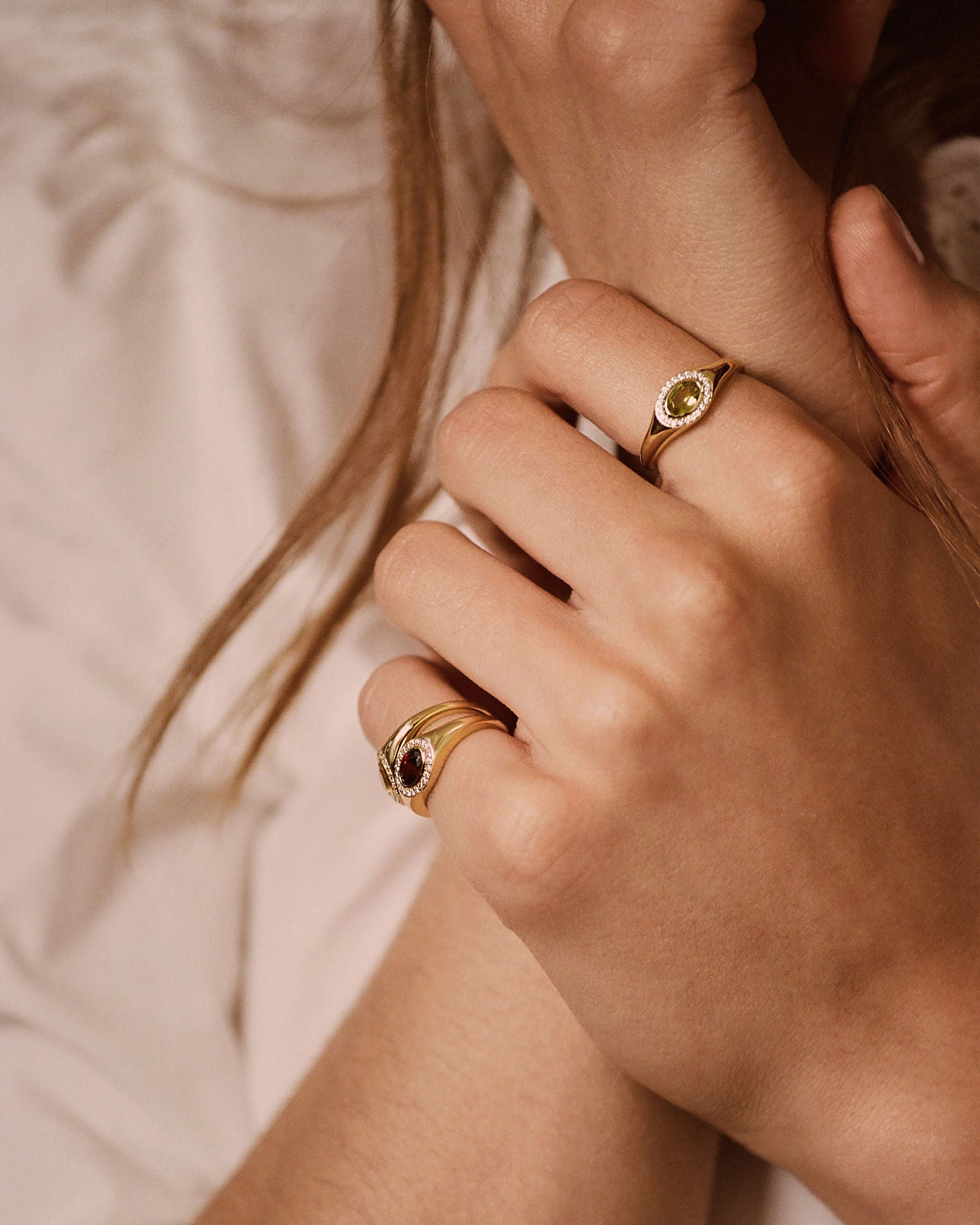 Close-up of a person's hands wearing gold rings, including one ring with a crescent moon and star design and another with a dark oval stone, set against a soft beige background.