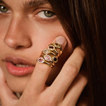 A close-up lifestyle shot of a model wearing a gold ring with multiple stacked oval gemstone settings on her finger.