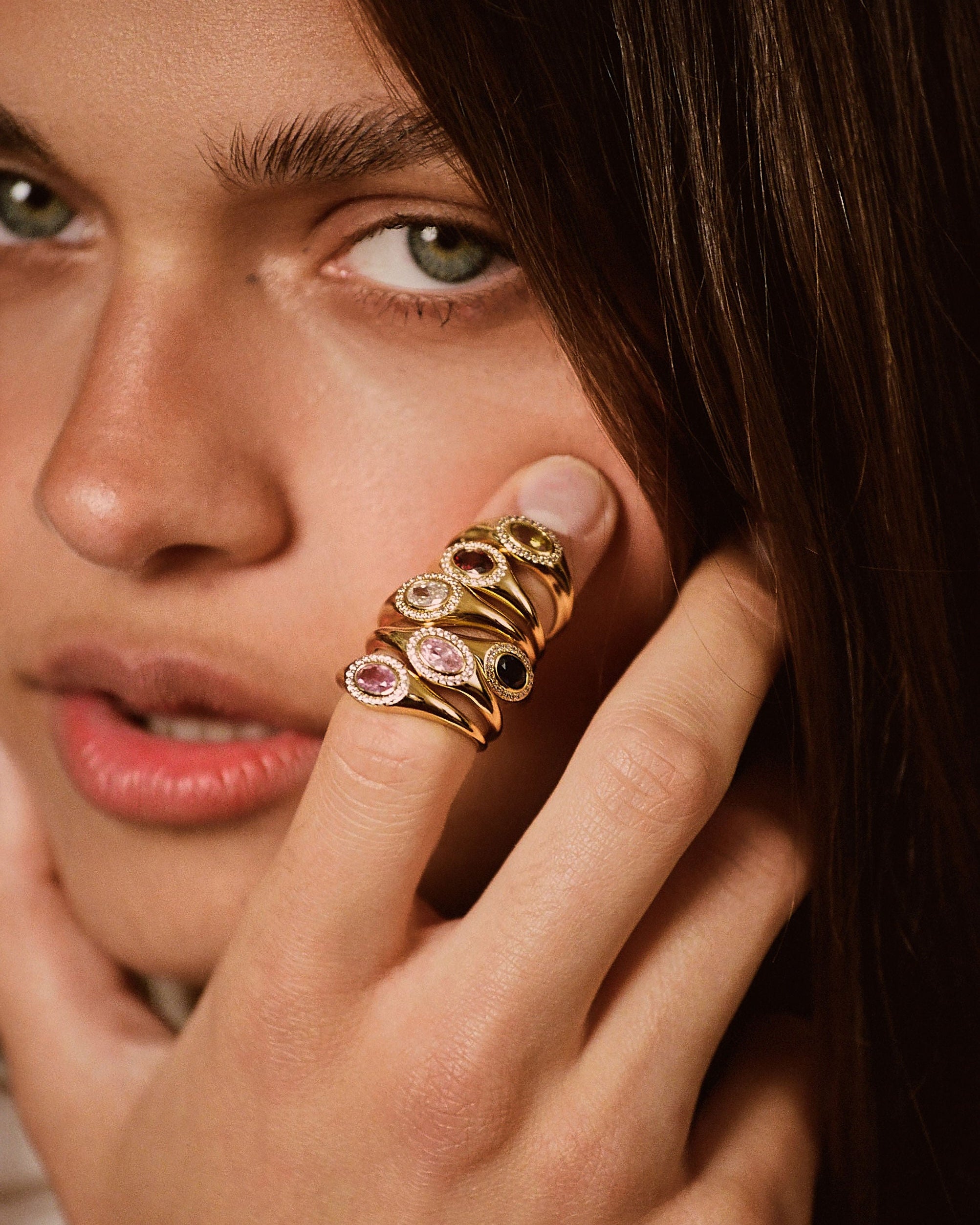 A close-up lifestyle shot of a model wearing a gold ring with multiple stacked oval gemstone settings on her finger.