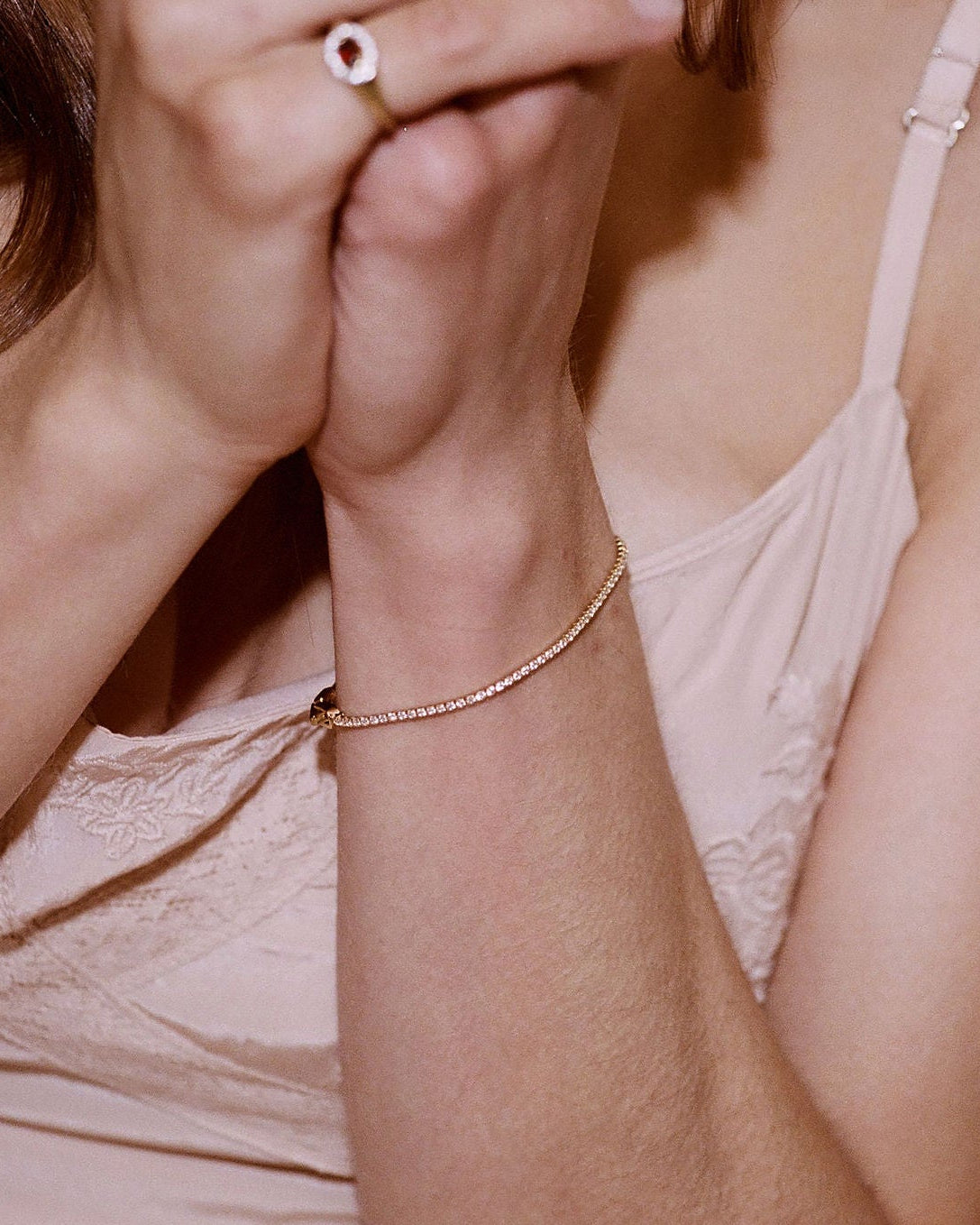 A delicate rose gold chain bracelet worn on a woman's wrist, shown in a close-up lifestyle shot with her hands clasped in front of her face.