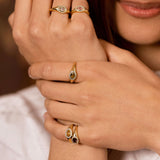 A close-up lifestyle shot of a model's hands wearing multiple gold rings with oval-cut stones, including a green stone and a dark red stone.