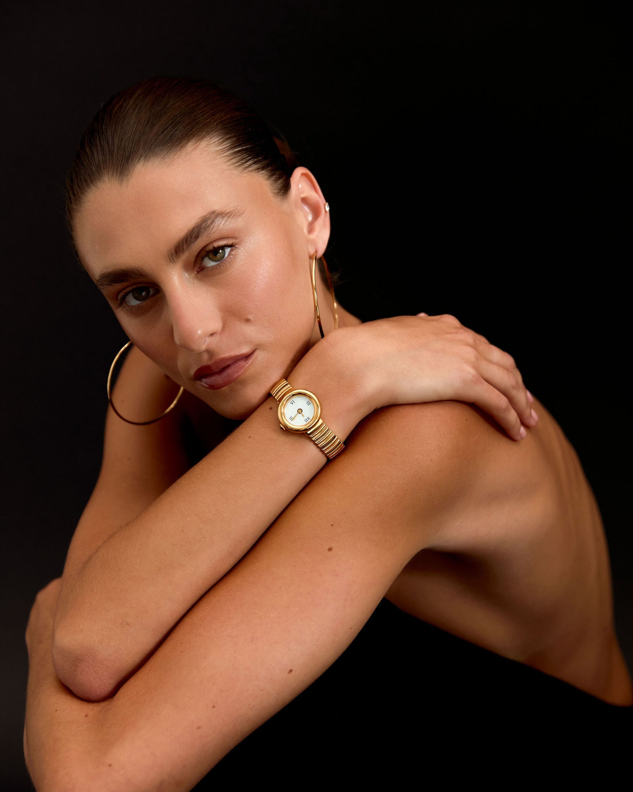 Woman wearing a gold watch on a black background