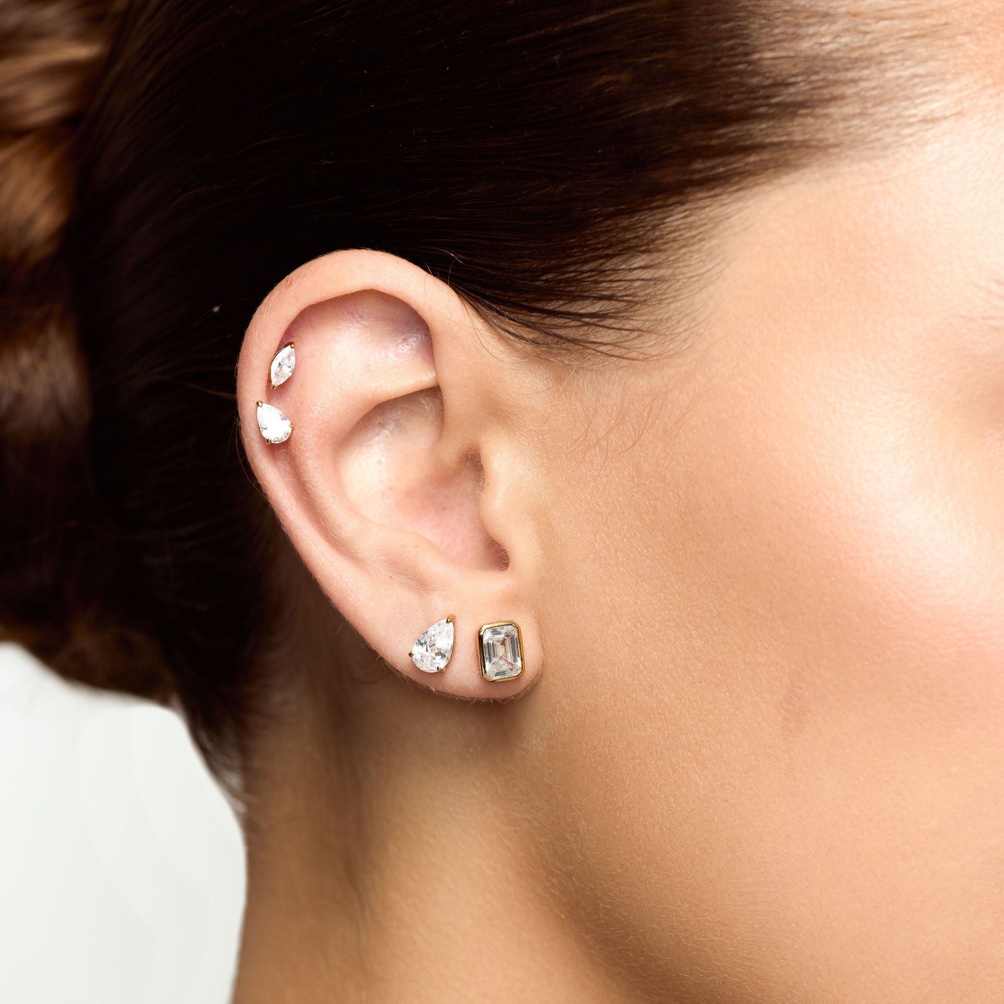 Close-up of a person's ear with multiple earrings on a neutral background
