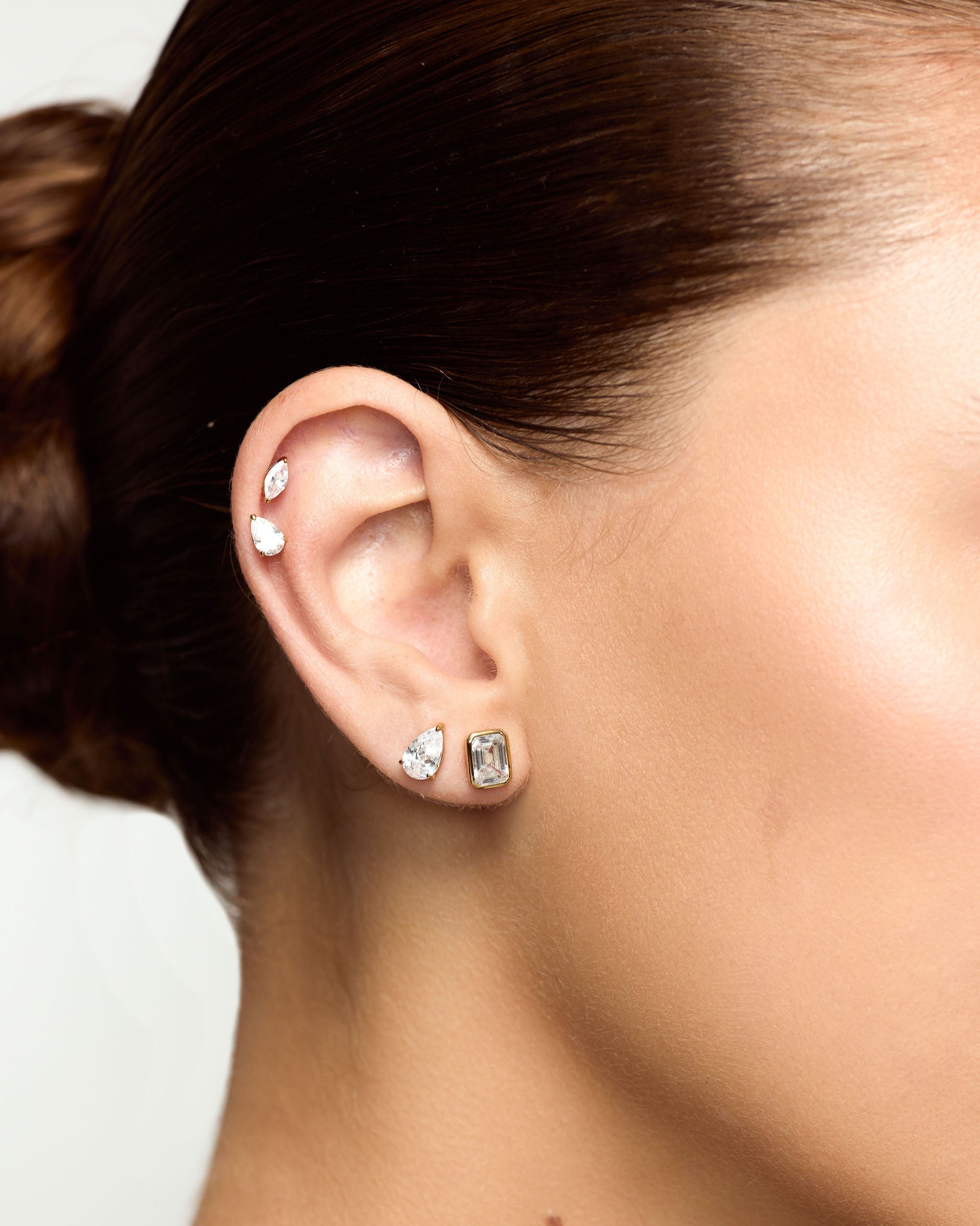 Close-up of a person's ear with multiple earrings on a neutral background