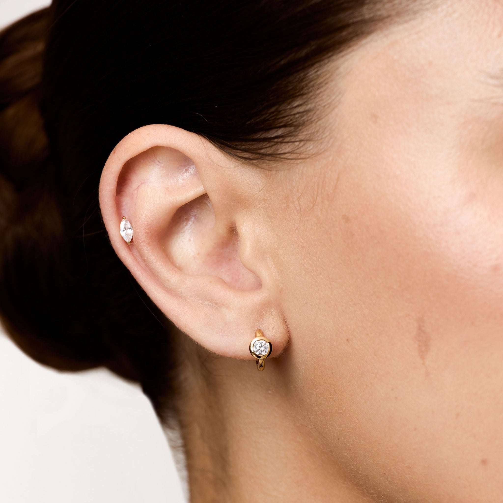Close-up of a person wearing diamond stud earrings with a neutral background