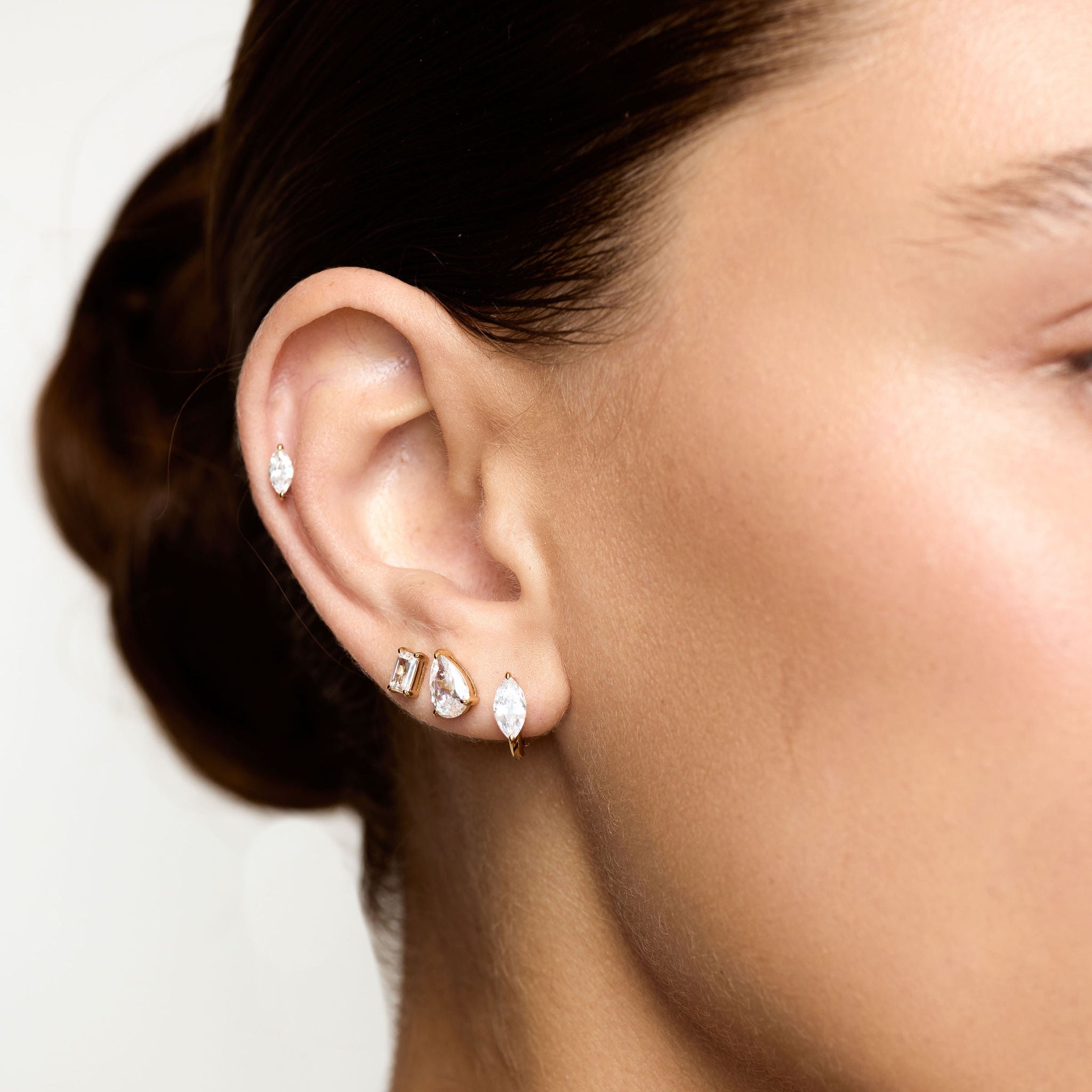 Close-up of a person wearing multiple earrings on a plain background