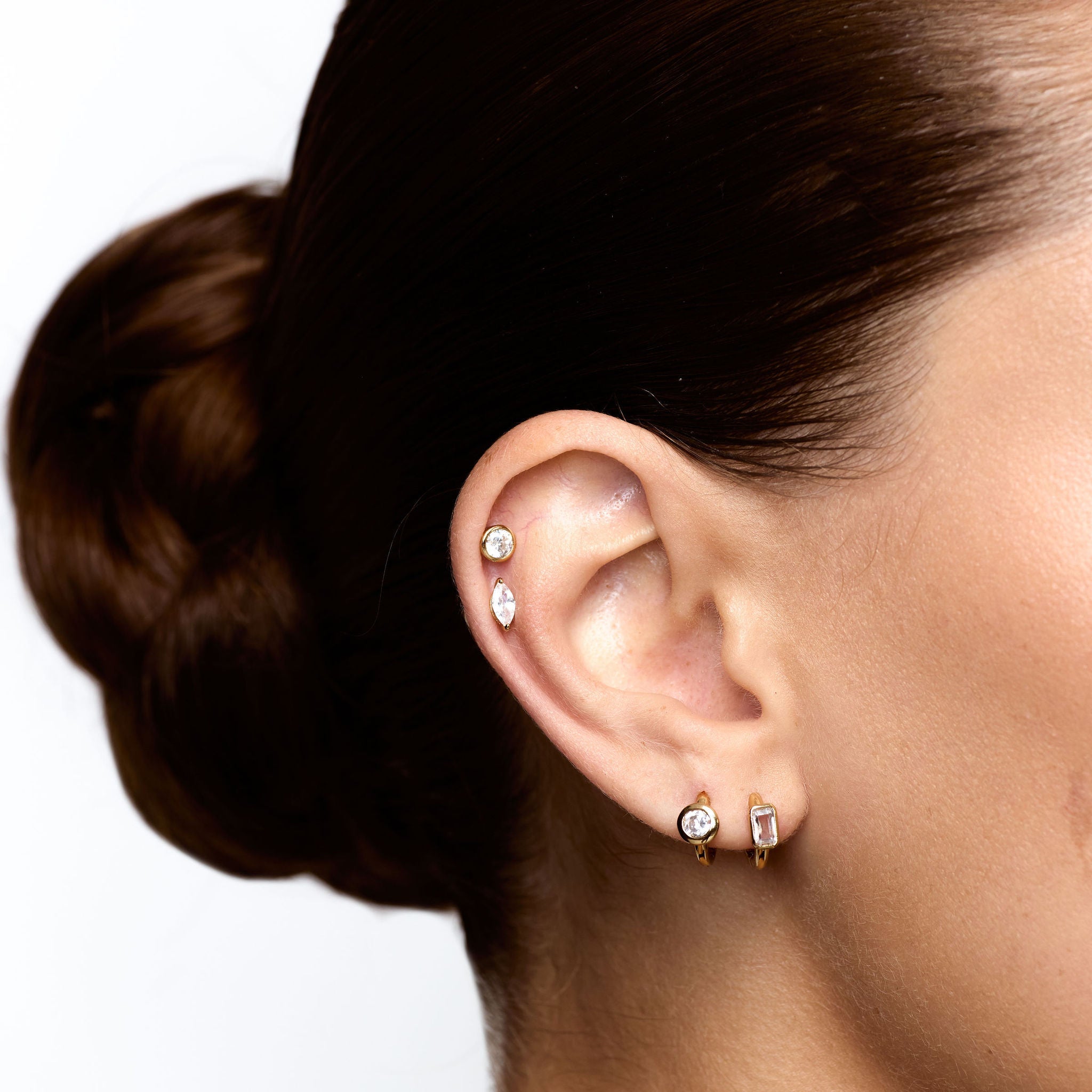 Close-up of an ear with diamond stud earrings on a white background