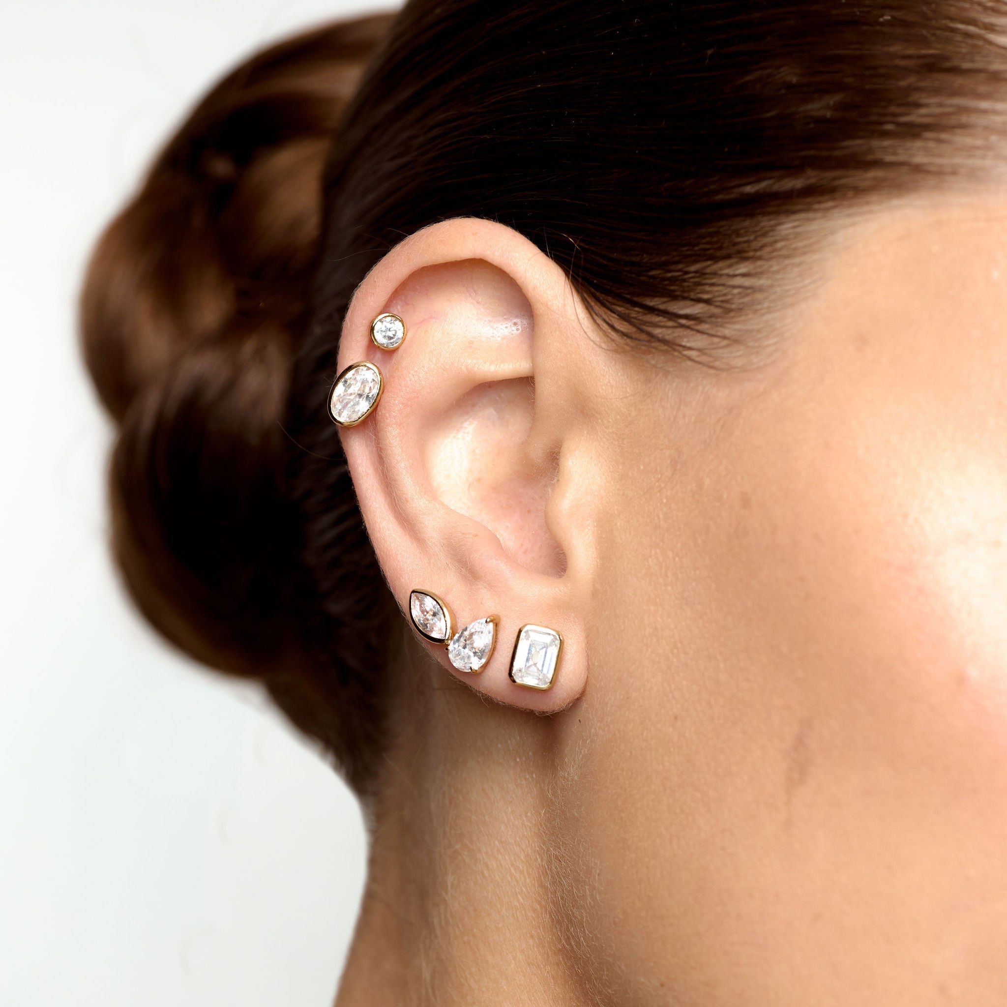Close-up of an ear with multiple diamond earrings on a plain background