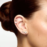 Close-up of an ear with multiple earrings against a neutral background