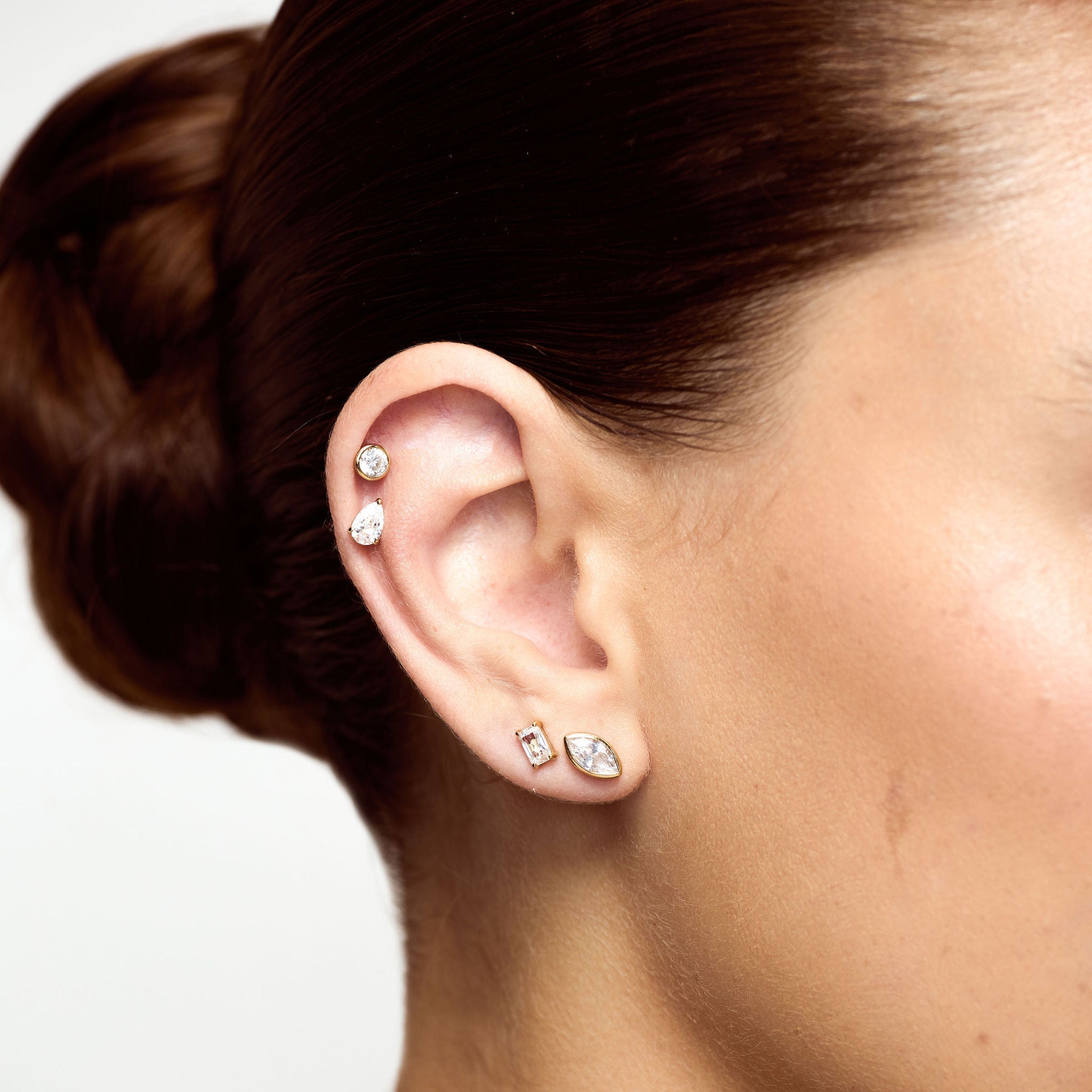 Close-up of an ear with multiple earrings against a neutral background