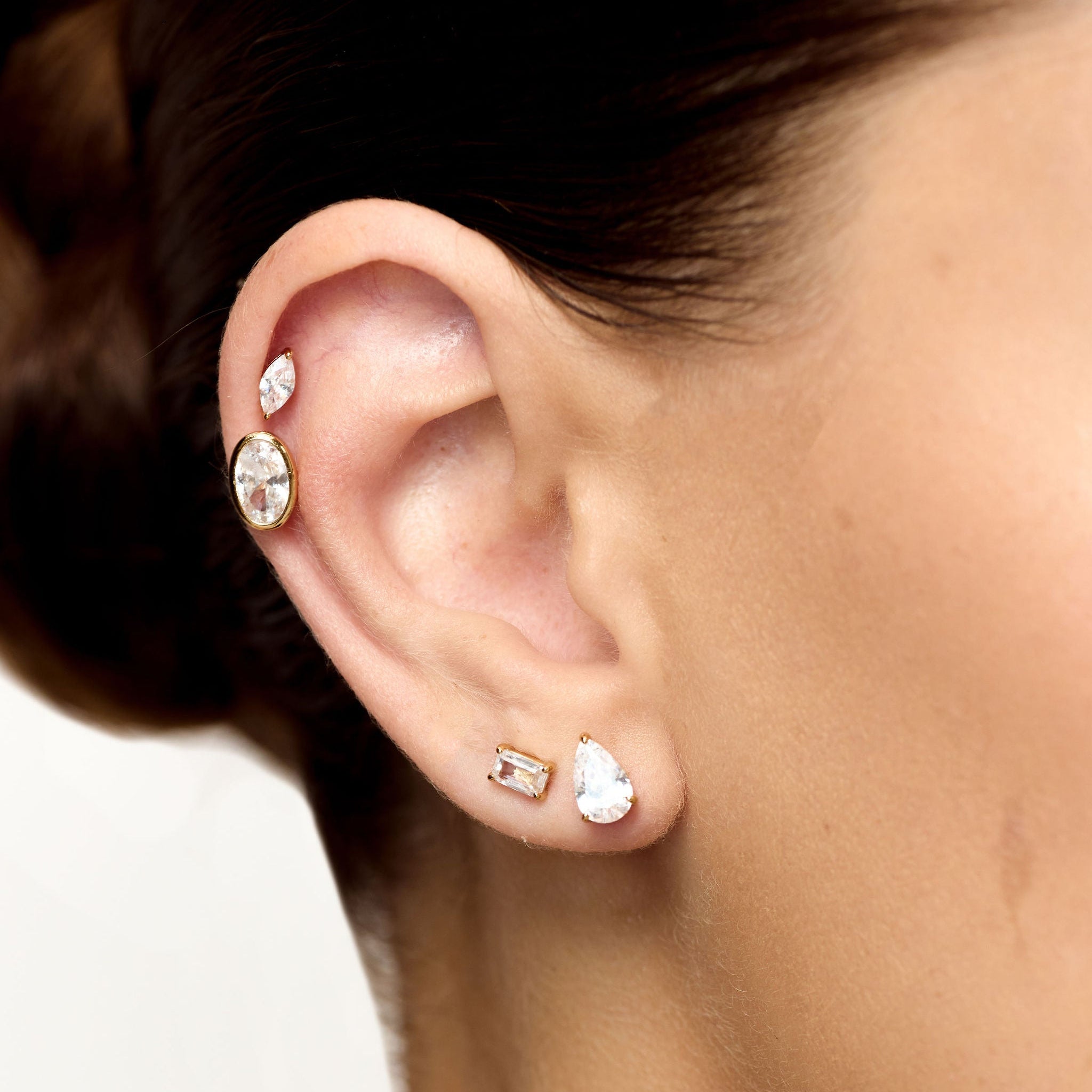 Close-up of an ear with multiple diamond stud earrings on a neutral background