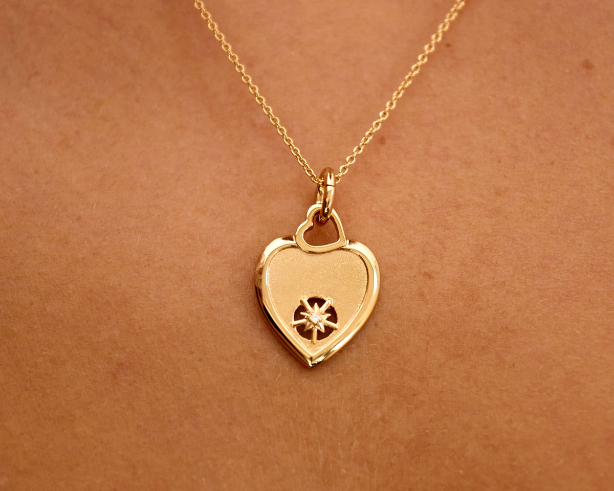 Gold heart-shaped necklace with a pendant on a person's neck against a brown background