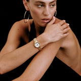 Woman wearing a gold watch and hoop earrings on a black background