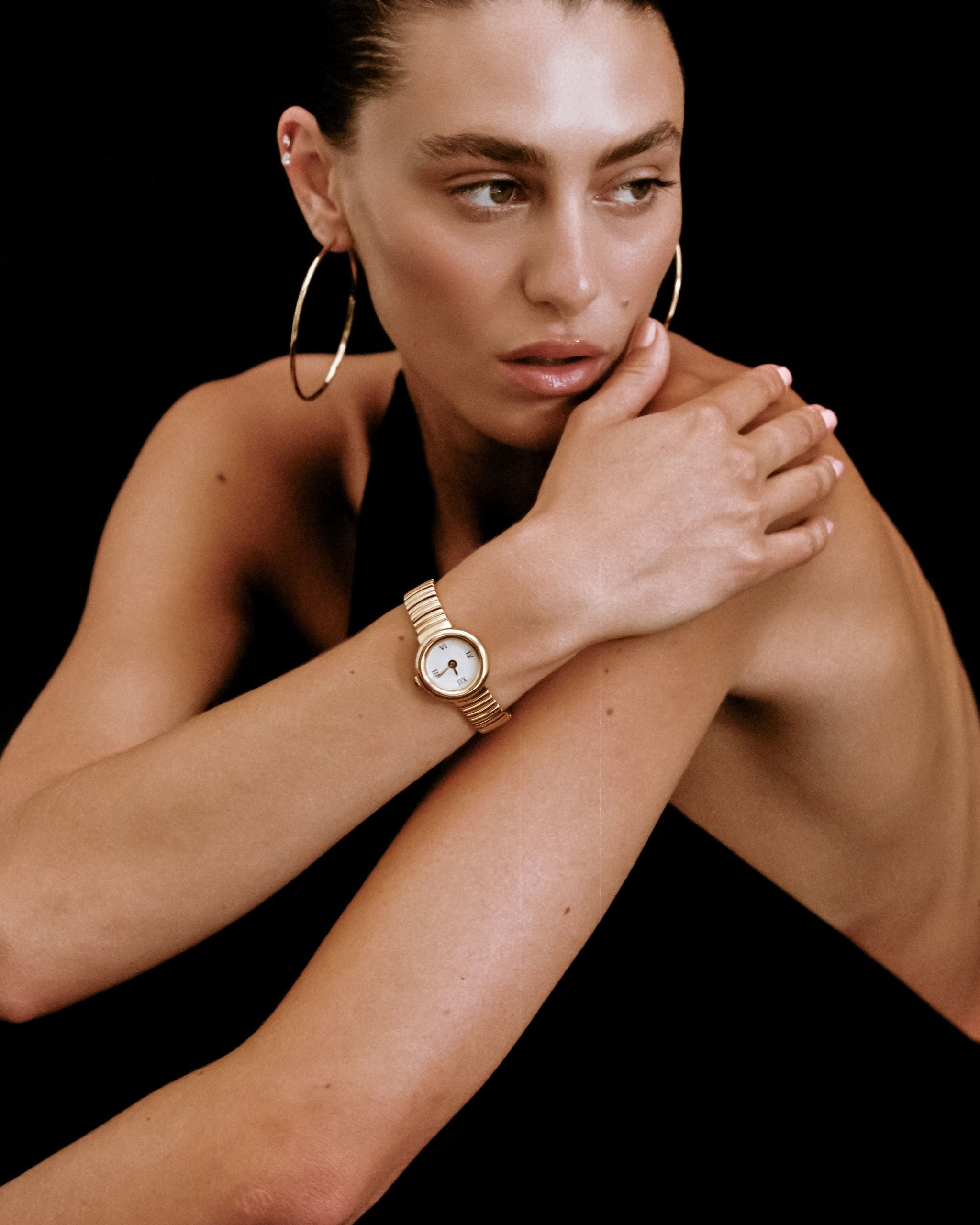 Woman wearing a gold watch and hoop earrings on a black background