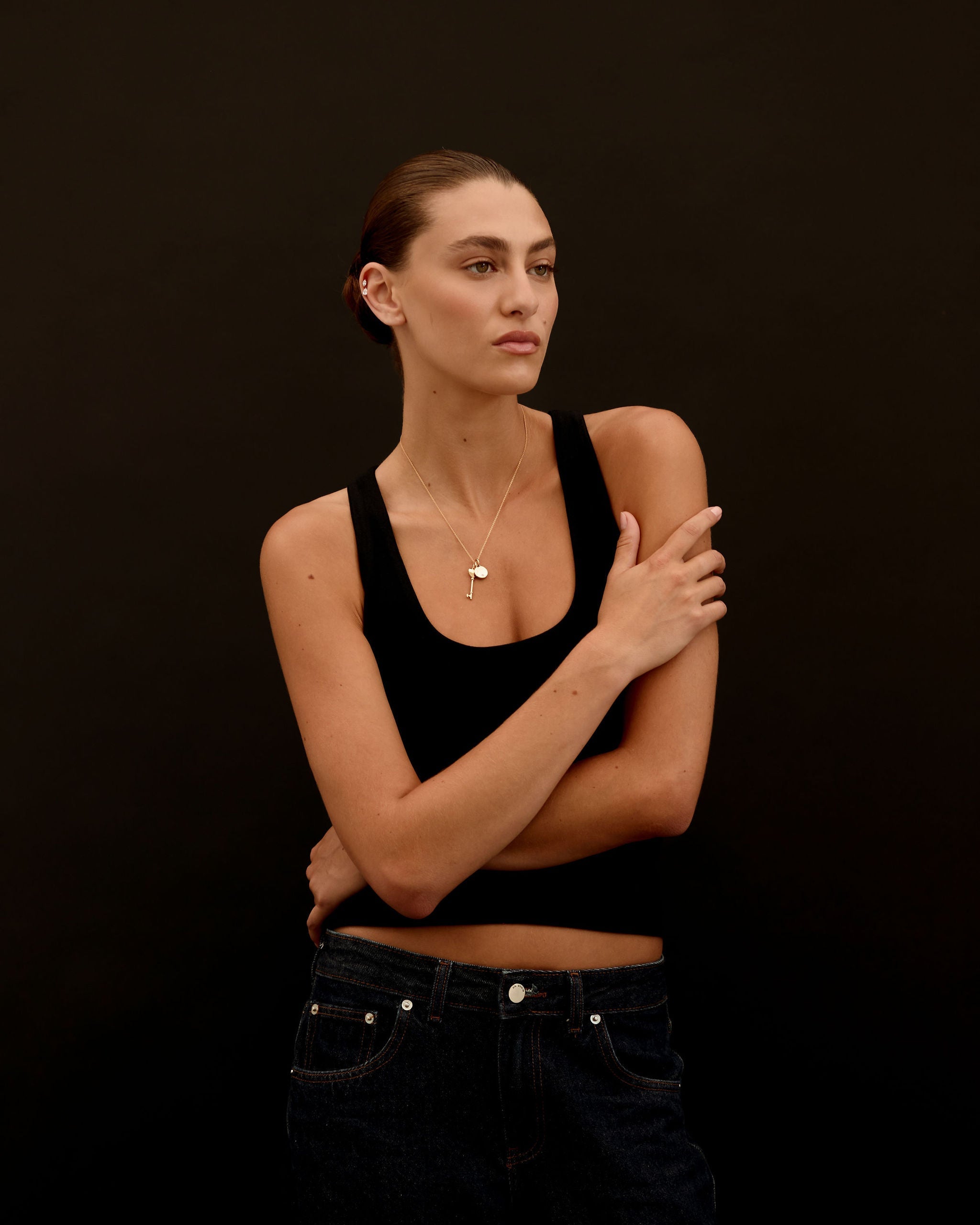 Person wearing a black tank top and jeans against a dark background