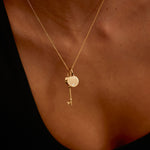 Gold necklace with a key pendant on a person's neck against a dark background
