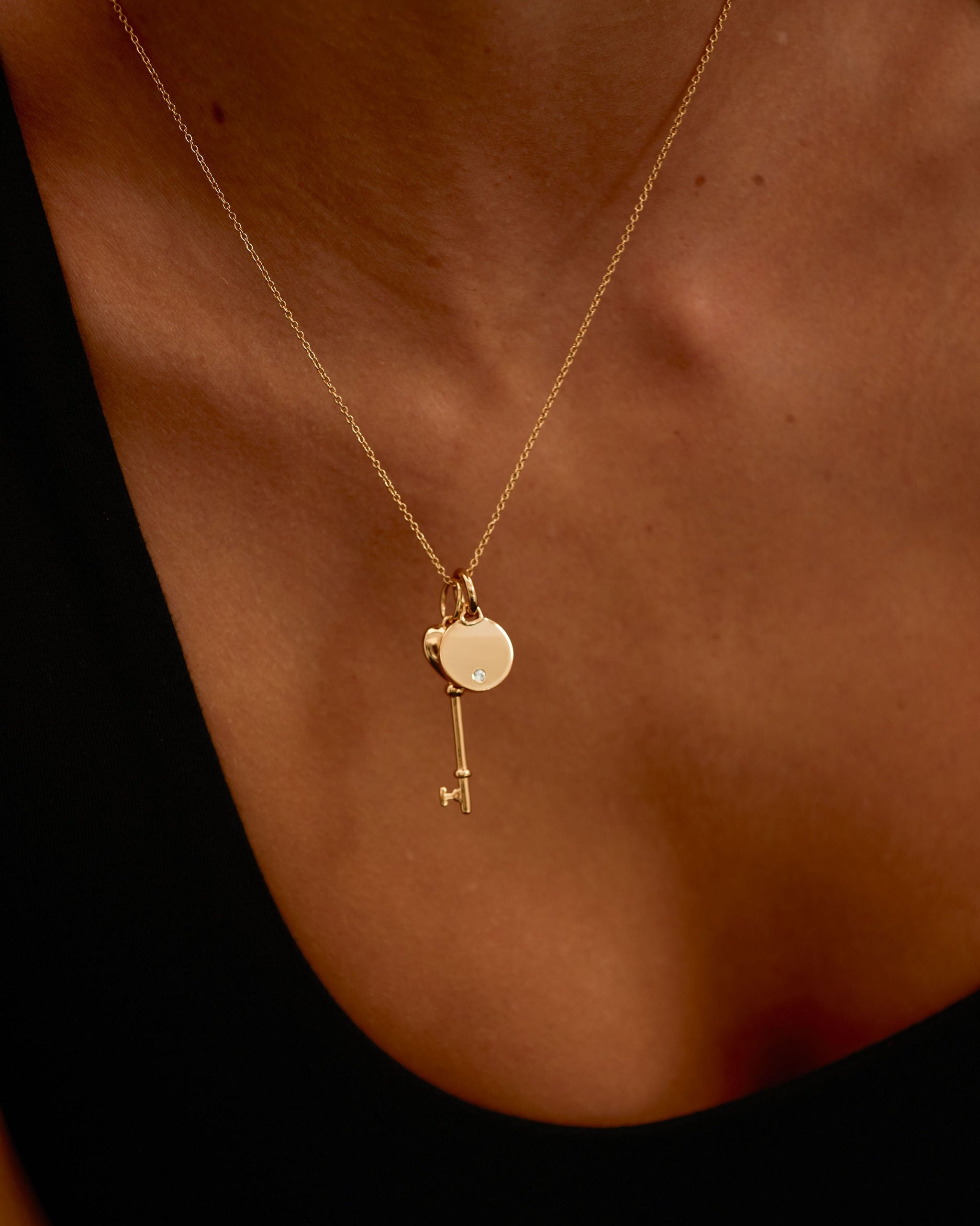 Gold necklace with a key pendant on a person's neck against a dark background