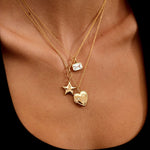 Gold necklace with star and heart pendants on a person's neck against a black background