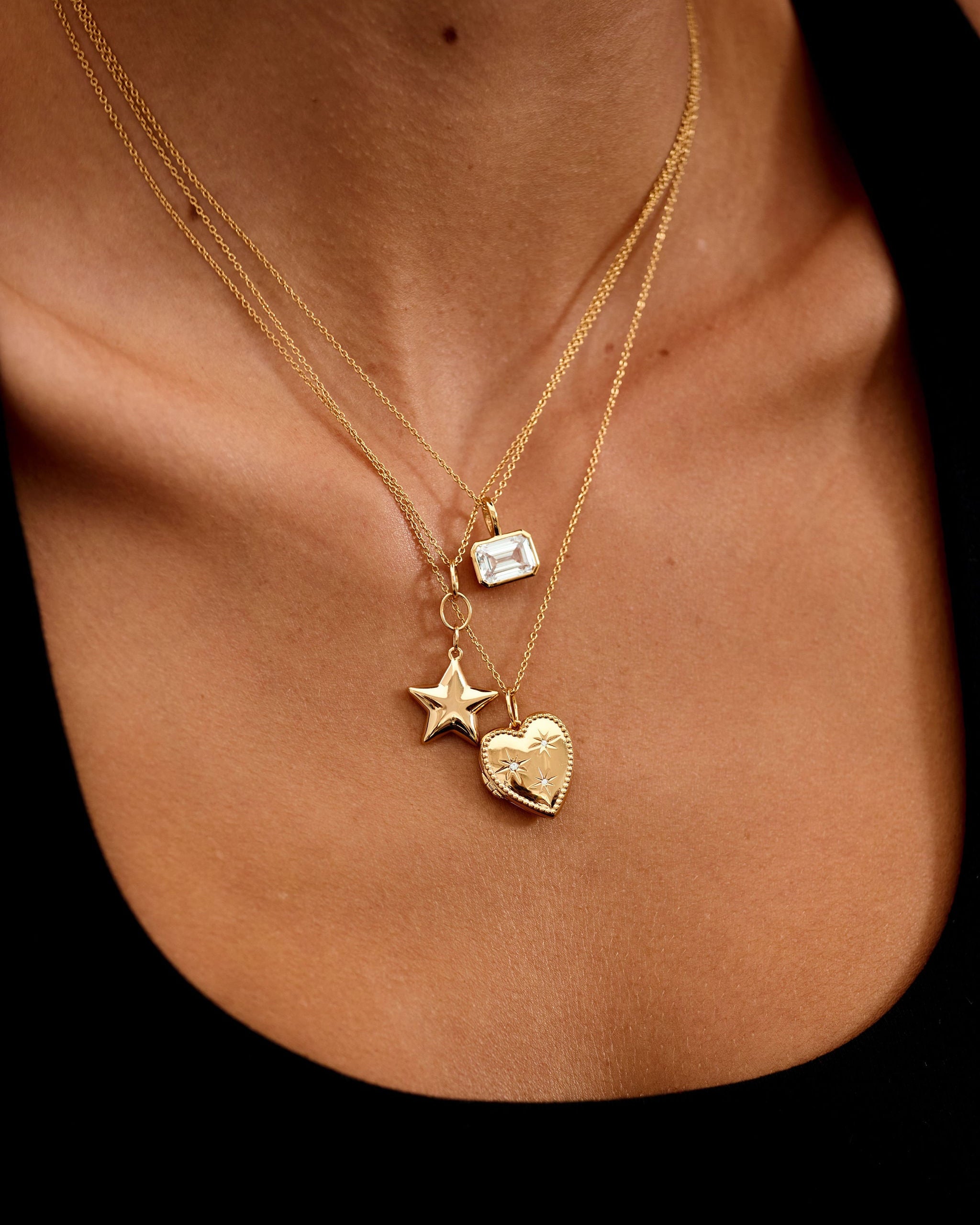 Gold necklace with star and heart pendants on a person's neck against a black background