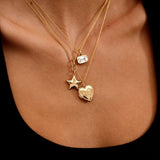 Gold necklace with star and heart pendants on a person's neck against a black background
