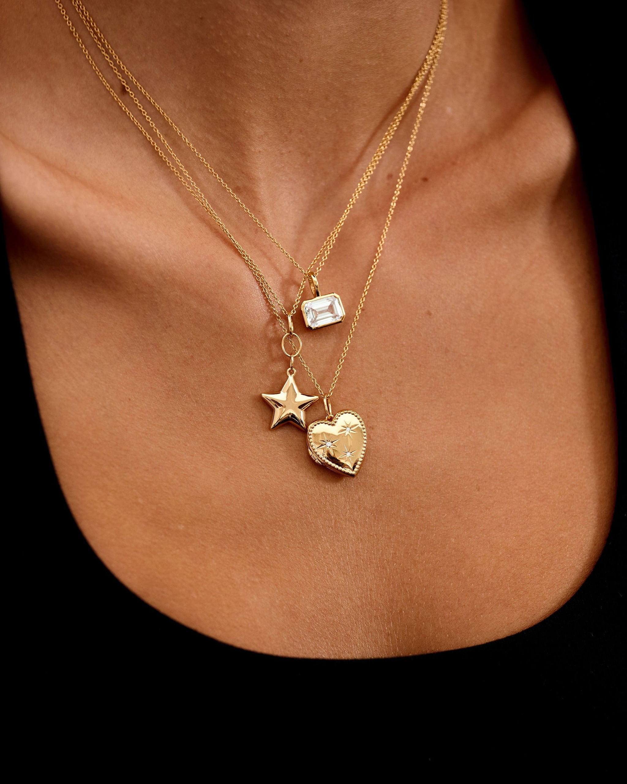 Gold necklace with star and heart pendants on a person's neck against a black background