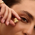 Close-up of a person wearing a gold heart-shaped earring.
