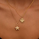 Gold necklace with a clover and star pendant on a person's neck.